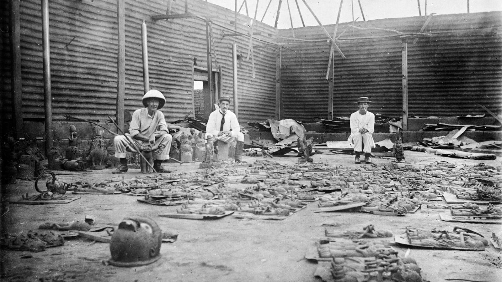 Interior of Oba's Compound Burnt During Seige of Benin City (present day Nigeria), with Bronze Plaques in the Foreground and Three British Soldiers of the Benin Punative Expedition 9-18 February 1897. Photographer Reginald Granville